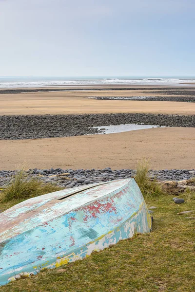 An upturned small boat washed up on the shoreline of a beautiful unspoiled beach