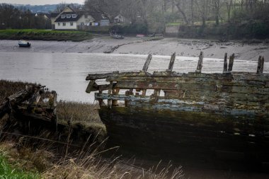 Kıyıya vurmuş eski bir ahşap tekne dökülüyor ve sular çekilince çürüyor.