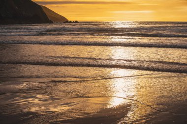 Sahilden denize bakan bir manzarada, suyun üzerinde parıldayan güneş ışığı yansımaları.