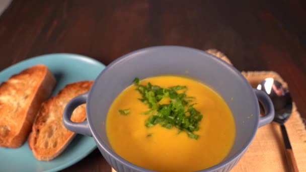 A bowl of homemade orange pumpkin soup on the table, sprinkle with chopped herbs. Toasted bread. — Stock Footage Bowl Homemade Orange Pumpkin Soup Table Sprinkle Chopped Herbs Toasted Video Clip