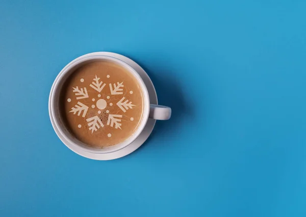A Cup of coffee with milk in a blue mug on a blue background, and the silhouette of a Christmas tree on the foam, flat lay, copy space. Christmas concept.
