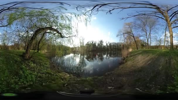 Mann klettert auf Hügel sphärisches Panorama Video Backpacker spaziert am See Fluss im Wald kahle Äste sonnig Frühlingstag blauer Himmel kleiner Planet Video — Stockvideo
