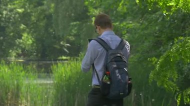 Man Clicks Park Akıllı Telefon Ekran Holding Bir Cep Telefonu Backpacker Etrafında Döner Doğa Taze Yeşil Ağaçlar Sunny Yaz Günü Yürüyor
