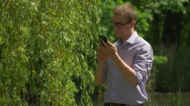 Adam cep telefonu Park'ta taze yeşil ağaçların göl su söğüt dalları kavak pamuk güneşli yaz adam tarafından geçen bisikletçi bakarak kaydırır