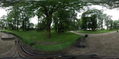 360vr Video adam tarafından yeşil ağaçlar altında patika Park banklar parlak sarı ceket turist Backpacker bulutlu sokakları binaları erkek bir Bisiklete binmek