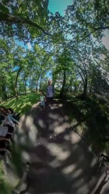 360vr Video adam alarak Video şehir gün Opole kamerada bir sopa baba yürüyüş ile onun kızı insanlar çocukların Botanik Bahçesi sokak güneşli yeşil ağaçların yanında yürüyor