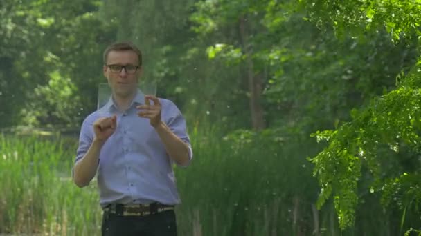 バーチャルタブレットを持つ男は、はい成功したビジネスマン外国為替インターネットショッピングチャット緑の木の近くに立って携帯電話を持って言う晴れ — ストック動画