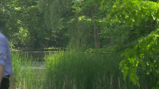 L'homme clique Smartphone se promène dans Green Park bavarder sur un téléphone portable Passez du temps à la nature Arbres verts frais Lac Acacia peuplier coton ensoleillé été — Video