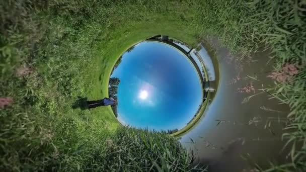 360vr Video Man pratar på telefon sitter ner gröna fält bro genom floden Reed av vatten turisten har en vila på natur sommaren middagstid Sunny Blue Sky — Stockvideo