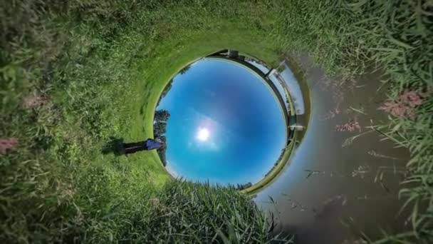 360Vr Video Uomo Parlando al telefono si siede Green Field Bridge attraverso il fiume Reed dal turista acqua ha un riposo alla natura Estate Mezzogiorno Sunny Blue Sky — Video Stock