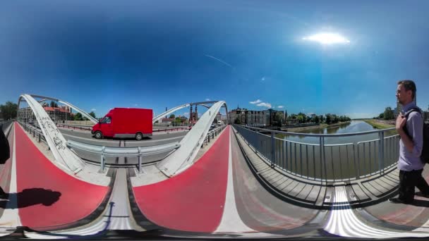 360vr videóinak hátizsákos séta a híd piros kerékpár Lane autók hajtja a Road-ember a mobiltelefon keresi a kamera nap süt fényesen nyári — Stock videók