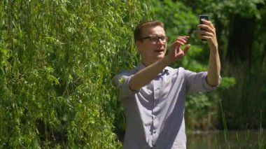 Dostum yapar Video seslenmek üstünde hareket eden telefon Park alır bir fotoğraf ekran zaman harcıyor doğa yeşil ağaçların göl su tıklama söğüt dalları güneşli yaz