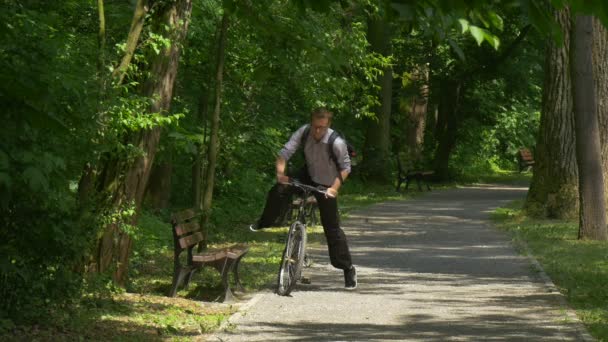 人就得在一辆自行车骑在绿色公园自行车运动员戴眼镜的年轻男子花时间在自然公园巷新鲜绿树阳光明媚夏日 — 图库视频影像
