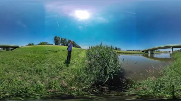 360Vr Video Hombre Hablando por Teléfono Caminando por Campo Puente a Través del Río Reed por el Agua Turista Descansa en la Naturaleza Verano Mediodía Sol Brilla Cielo Azul — Vídeos de Stock