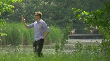 Panoramik fotoğrafta adam cep telefonu Green Park ile bir akıllı telefon tutarak ve döndürme kavak pamuk ağaçlar güneşli yaz uçan doğa zaman harcamak