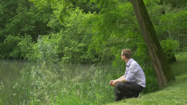 Geschäftsmann sitzt im Park mit virtuellem Tablet Devisenhändler Internet-Shopping am Seeufer Mann hält ein Tablet Blick auf Wasser frische grüne Bäume Sommer — Stockvideo