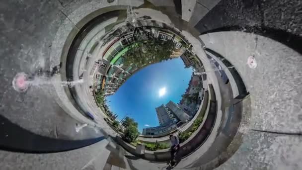 Vidéo 360Vr Touriste assis près d'une fontaine Ville Backpacker Paysage urbain Voitures sont conduits par la route Maisons multi-étages Soleil brille Ciel bleu Arbres verts — Video