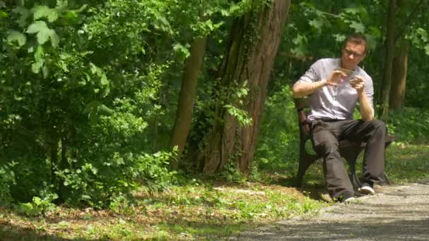 Hombre con la tableta en Green Park se inclina a la banca detrás de chatear Forex Bienes Raíces Comprar Internet Compras Pasar tiempo en la naturaleza árboles verdes frescos — Vídeos de Stock