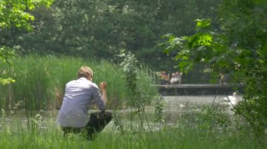 Adam cep telefonu ile bir taş içine Gölü yeşil Park doğa taze yeşil ağaçlar güneşli yaz gününde bir akıllı telefon arama harcamak zaman Holding kadar alır atar