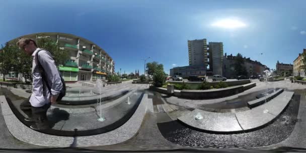 360vr wideo Backpacker spaceru wzdłuż fontanna turystycznych jest przenoszenie wokół gród samochody napędzane są przez Road budynków słońce świeci niebieski niebo zielone drzewa — Wideo stockowe