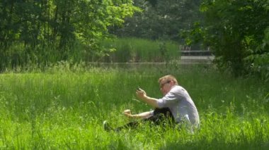 Adam cep telefonu ile yere oturur bir Smartphone ekran arama tıklama Holding Park doğa yaz zaman harcamak fotoğraf adam gözlük alarak