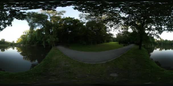 360vr 视频人走在沿着河流的城市公园的人行道上, 或者湖中的球面全景灯正在通过树枝闪耀 — 图库视频影像