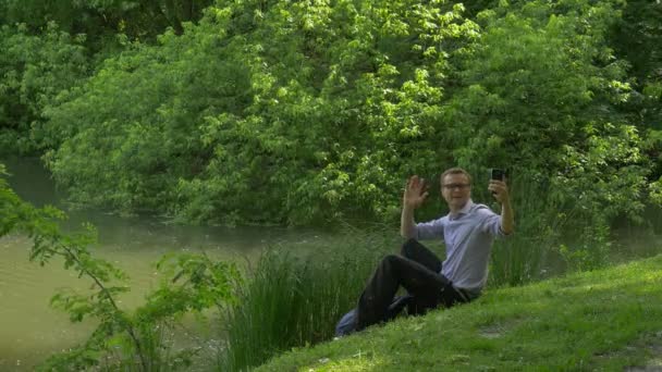 Businessman With Mobile Phone Sitting on Green Hill Holding a Smartphone Spends Time in Park Fresh Green Grass Trees Sunny Summer Day — Stock Video