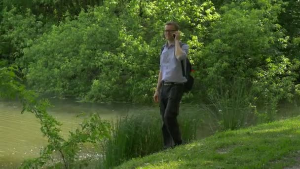 Geschäftsmann mit Handy auf grünem Hügel sitzend und Smartphone in der Hand verbringt Zeit im Park frisches grünes Gras Bäume sonnigen Sommertag — Stockvideo