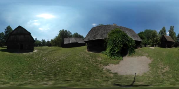 360vr Videotourist unter den Hütten alter Dorfbewohner läuft und beobachtet rustikale Häuser schleichende Pflanze auf der Tür Höfe grüne Bäume Rasen sonniger Tag — Stockvideo