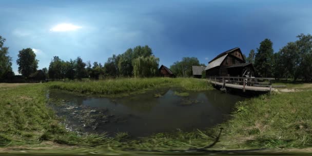 360Vr Homem de vídeo na ponte Cottage Water Mill Old Village Tourist está observando Rustic Lake House com seus pátios Árvores verdes Gramado Floresta Dia ensolarado — Vídeo de Stock