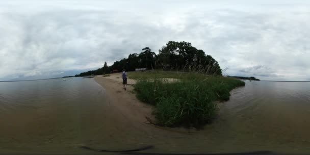 Відео людина 360vr на березі річки сферична Панорама перегляд на набережній озера або ставок Сенді згладити Limpid вода зелена трава похмурий день — стокове відео