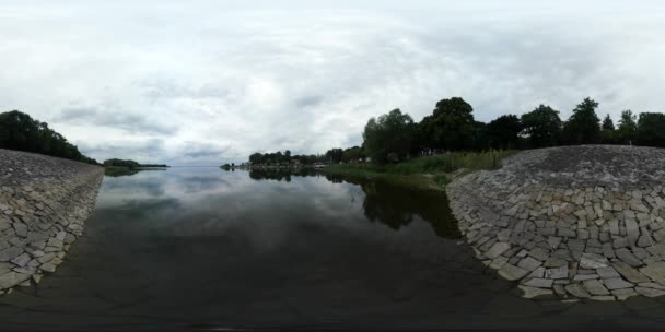 360Vr Video L'uomo riposa sulla riva rocciosa Wood Lake Tourist sta camminando lontano L'uomo tra gli alberi verdi selvatici su un orizzonte Smooth Water Sky Reflection Cloudy — Video Stock