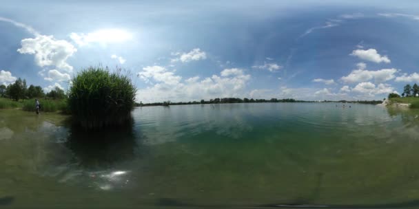 360vr Videomann fording ein Meer Bucht grünes Ufer des Flusses Schilf plätschert Wasser Küste Insel grüne Büsche Bäume Wolken schweben sonnigen Sommer — Stockvideo