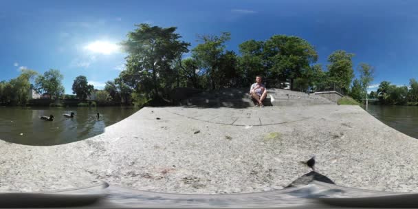 360Vr Video El hombre lanza un pan a las palomas pájaro Vienen Lago Embankment Las aves están caminando alrededor del hombre Recogiendo la comida Los patos se reúnen Día soleado — Vídeos de Stock