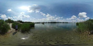 360vr Video adam ayakta su Gölü banka turkuaz şeffaf su Reed ağaçlar adama doğa yürüyüşleri uzak bulutlar güneşli yaz gün Blue Sky adlı arıyor