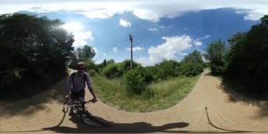 360vr Video adam Bisiklet alarak Video kullanarak at binme bir Selfie sopa yol yapılmış, parke döşeme Backpacker sürme yoluyla Park Yaz manzara güneşli olduğunu