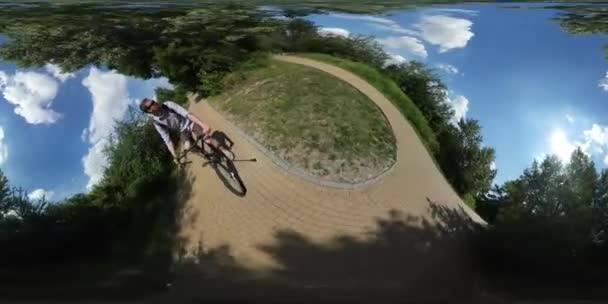 360Vr Video Hombre está montando una bicicleta tomando vídeo utilizando un camino de palo selfie hecho de pavimentación azulejos mochilero se detiene cerca de Turquoise Lake Park Día soleado — Vídeos de Stock