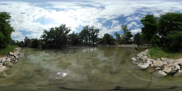 360Vr видео человек фординг озеро в парке Зеленые деревья банк награжден Камни турист отдыхает на природе в облачные летний день — стоковое видео