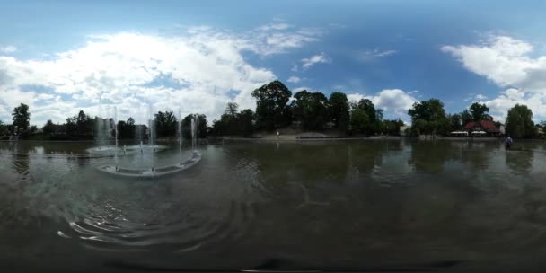 360vr 视频背包客在夏季日在银行红顶背包客旅游的池塘公园绿树倒楼的浅层喷泉 — 图库视频影像