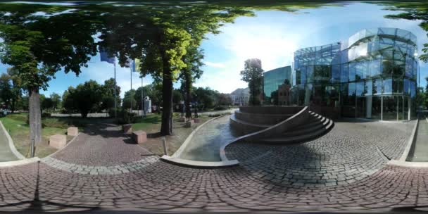 Vídeo 360Vr que pavimenta pedras no edifício de vidro moderno quadrado no parque Árvores verdes Dia ensolarado Bandeiras ucranianas e polonesas estão acenando bancos no beco Cityscape — Vídeo de Stock