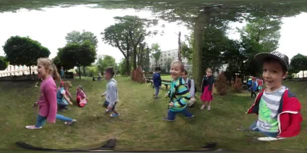 Vídeo de 360Vr Crianças do jardim de infância que caminham pela câmera As crianças estão sorrindo Brincando na grama Meninos e meninas em um bom dia ensolarado de humor — Vídeo de Stock