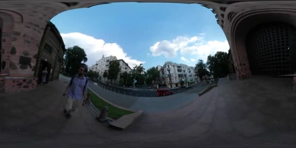 360vr video man walking through golden gate kiev city day downtown old building cars are driven people are walking by the city square green grass summer — Stockvideo