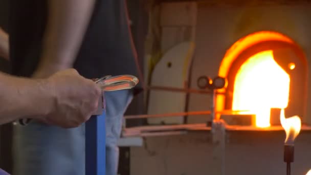Человек придает круглую форму к украшению стекла с помощью металлических инструментов — стоковое видео