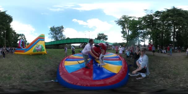 Vídeo de 360Vr Crianças montando no divertimento inflável do touro Os pais no campo de jogos A mãe ajuda seu filho a usar um sapato As famílias passam tempo juntas Green Grass Park — Vídeo de Stock