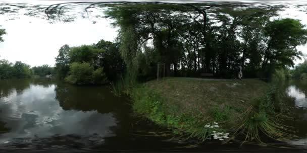 360Vr Vídeo Homem Obtém em um passeio de bicicleta por Alley Park Rippling Water Forest Lake Green Trees Summer Man Passe o tempo na natureza bela paisagem — Vídeo de Stock