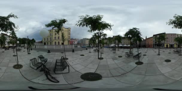 360vr Video Menschen laufen über den Platz aus Pflastersteinen junge Bäume Fahrrad in der Nähe von Bänken in Parkautos Stadtbild Gebäude am Horizont — Stockvideo