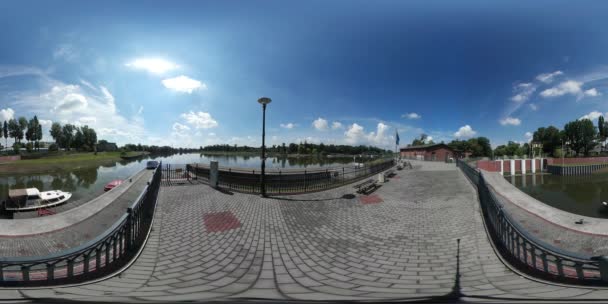 360Vr Video Hombre de pie en el muelle del lago Embankment Plaza hecha de azulejos de pavimentación Valla decorativa Cielo Reflejo en un árbol de agua en un horizonte Día de verano soleado — Vídeo de stock