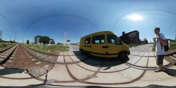 360Vr Vidéo Homme Marcher lentement Traversée Gare Ferroviaire Bâtiments Voitures Ensoleillé Journée d'été Pelouses Vertes Traversée de chemin de fer en gravier — Video