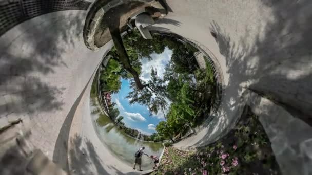 360 Degree Rabbit Hole Planet Family Park Embankment People at Small Lake Among the Trees Flower Beds Green Fresh Trees Paving Stones Blue Sky White Clouds — Stock Video