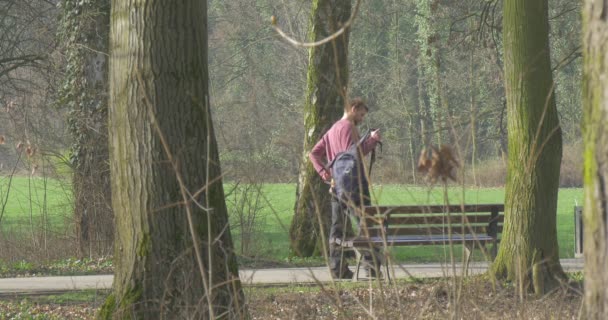 Молодой человек прогуливается по городскому парку — стоковое видео